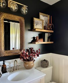 a white toilet sitting under a bathroom mirror next to a wooden shelf filled with flowers