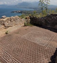 a mosaic on the ground in front of some rocks and water with mountains in the background