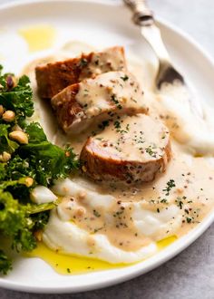 a white plate topped with meat covered in gravy next to broccoli