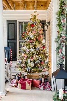 a christmas tree with presents under it in front of a house decorated for the holidays