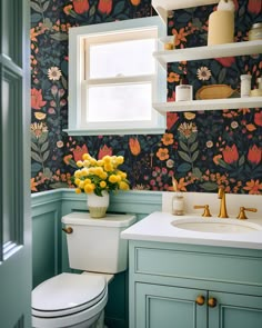 a white toilet sitting next to a bathroom sink under a window with flowers on it