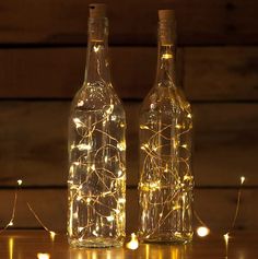 two bottles with fairy lights in them on a table