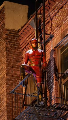 a man in a red suit standing on top of a fire escape ladder next to a brick building