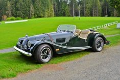 an old fashioned sports car parked on the side of a road in front of a golf course