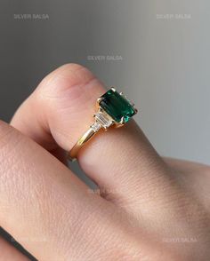 a woman's hand holding an emerald and diamond ring