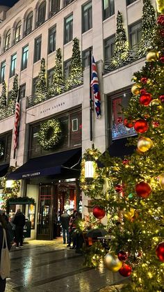 a christmas tree in front of a building with lights and decorations on the trees outside