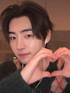 a man making a heart with his hands while listening to music on earphones in front of him