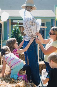 a group of people standing next to each other in front of a scarecrow on hay