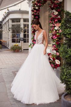 a woman in a white wedding dress standing on the sidewalk with pink flowers behind her