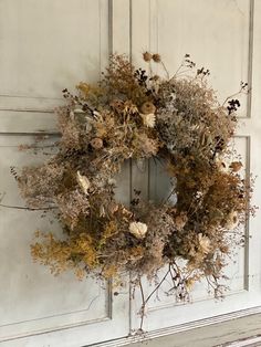 a wreath is hanging on the door with dried flowers and leaves around it in front of an old wooden door