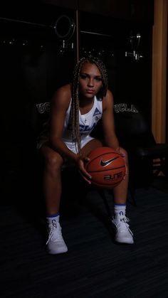 a woman holding a basketball sitting on top of a wooden floor next to a wall