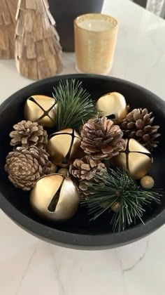 a black bowl filled with pine cones and gold ornaments on top of a white table