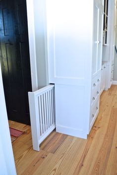 an empty hallway with white furniture and wood flooring in front of a black door