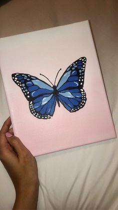 a hand is holding a pink and blue butterfly on a white canvas with black dots