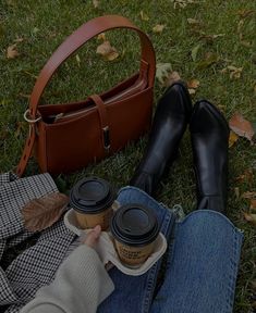 a woman is sitting on the grass with her purse and coffee