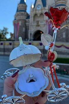 a person holding up a fake flower in front of a castle with a red rose on it