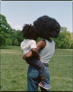 a woman holding a child in her arms while standing on top of a lush green field