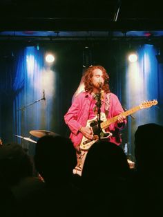 a man with long hair and beard playing guitar in front of an audience at a concert