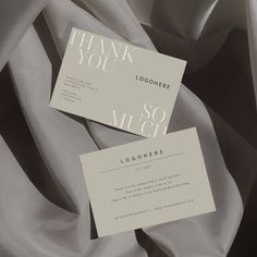 two thank you cards sitting on top of a bed covered in grey sheets and silk