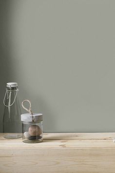 two glass jars with rocks in them sitting on a wooden table against a gray wall