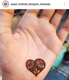 a small heart tattoo on the palm of someone's left hand, which is decorated with intricate designs