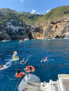 people swimming in the water near boats and cliffs