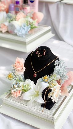 two black jewelry boxes with flowers and necklaces on them sitting on a white table cloth