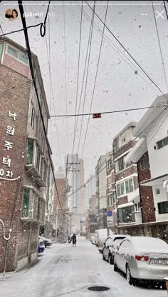 cars parked on the side of a snow covered street next to tall buildings and power lines