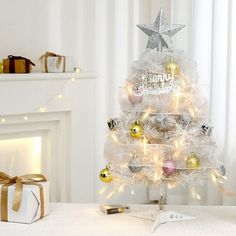 a white christmas tree decorated with gold and silver baubles, presents and lights