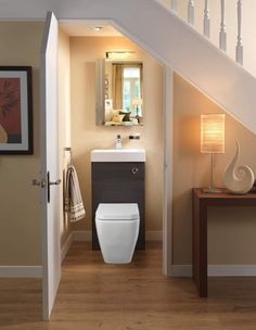 a white toilet sitting under a stair case next to a bathroom sink and mirror on top of a wooden floor