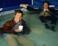 two men are sitting in the water and one man is holding a cup with his hand