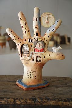 a ceramic sculpture of a hand with faces on it and two birds perched on the table