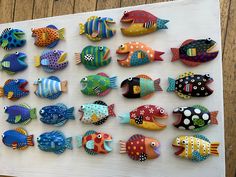 a group of colorfully painted fish sitting on top of a white board next to a wooden wall