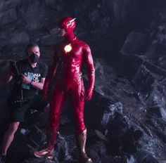 two men standing next to each other in front of a cave with rocks and water