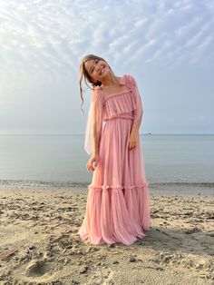 a woman standing on top of a sandy beach next to the ocean wearing a pink dress