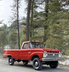 an old red pick up truck parked on the side of the road in front of some trees