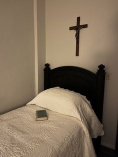 a bed with a cross on the wall above it and a book laying on top