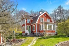 a red house with white trim on the front and side windows is surrounded by green grass