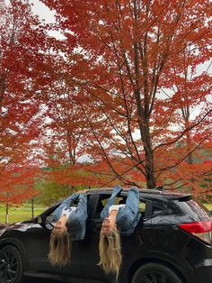 a woman laying on the back of a car in front of a tree with red leaves