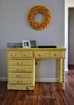 a yellow desk with drawers and a wreath on the wall