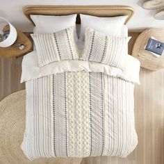 a bed with two pillows on top of it next to a wicker basket and lamp