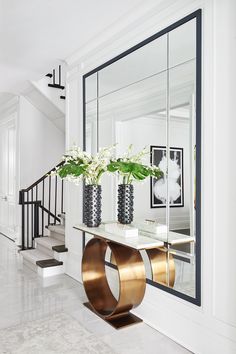 a vase with flowers sitting on top of a table next to a mirror and stairs