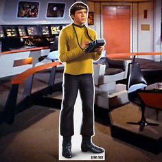 a star trek character holding a camera in a room with desks and chairs behind him