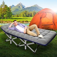 a man laying on top of a bed in the grass next to an orange tent