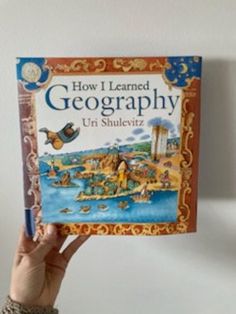 a person holding up a book about how i learned geography in shulevz