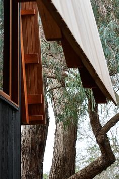 an open window on the side of a wooden house with trees in the foreground