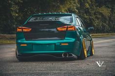 the rear end of a green car parked in a parking lot with trees behind it