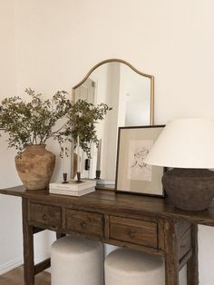 a wooden table topped with two white stools next to a mirror