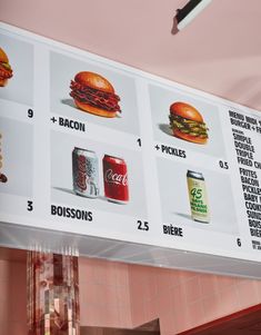 a menu hanging from the ceiling in front of a pink wall with different types of food on it