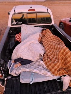 a person sleeping in the back of a truck with blankets on it's bed